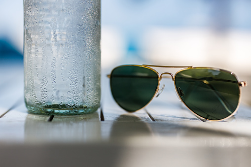 Close up of cold water bottle with dipping drops and sunglasses.