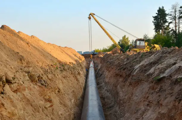 Photo of Natural gas pipeline construction work. A dug trench in the ground for the installation and installation of industrial gas and oil pipes