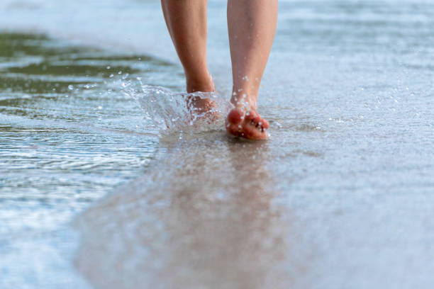 mujer descalzo caminando en la playa de verano. cerca de la pierna de la joven caminando a lo largo de la ola de agua de mar y arena en la playa. concepto de viaje. - barefoot behavior toned image close up fotografías e imágenes de stock