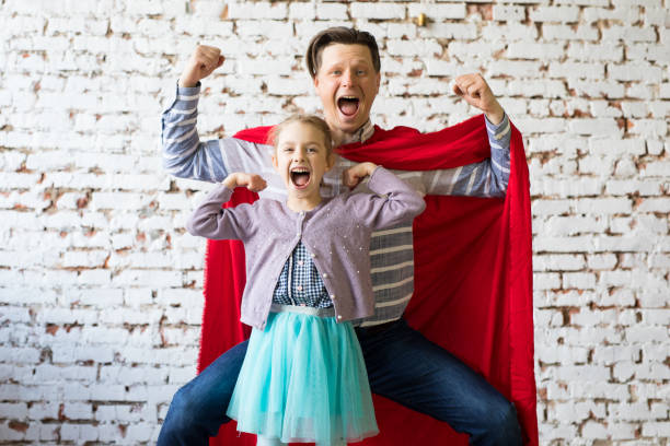 padre feliz en traje de superhéroe y su hija - action family photograph fathers day fotografías e imágenes de stock