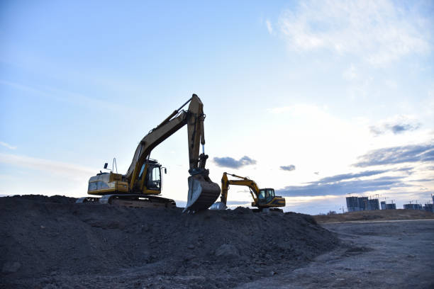 Excavators work at constrruction site on sunset background. Backhoe digs gravel and old concrete. Recycling old asphalt at a landfill for the disposal of construction waste. Construction machinery