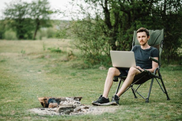 istock Man working on laptop online on nature. Young freelancer relaxing in forest. Remote work, outdoor activity in summer. Travel, hiking, technology, tourism, people concept. 1255901502