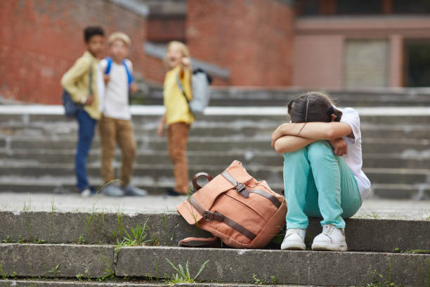 School Bullying Full length portrait of crying schoolgirl sitting on stairs outdoors with group of teasing children bullying her in background, copy space exclusion stock pictures, royalty-free photos & images