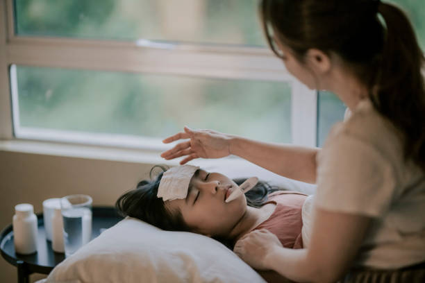 an asian chinese mother is taking care of her daughter on bed and measuring her body temperature with thermometer - offspring child lying on back parent imagens e fotografias de stock