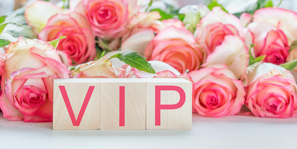vip sign by red letters on wooden blocks on table rose flowers background hotel service concept