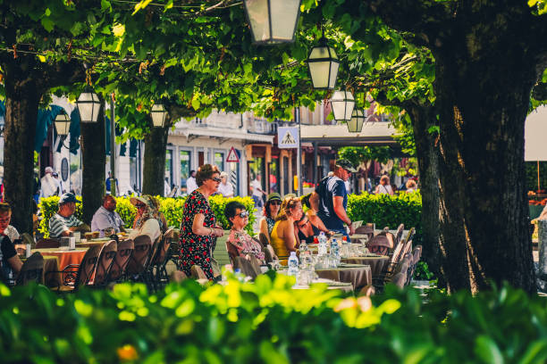 Bellagio, Italy - June 13, 2019: People on outdoor cafe terrace on quay of lake Como (Italian Lago di Como) in summer. Fashionable vacations and holidays. Lakeside restaurant. Picturesque place.