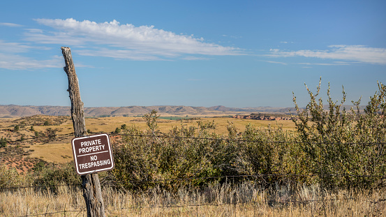 private property, no trespassing sign on barbed wire fence at Colorado foothills, fall scenery