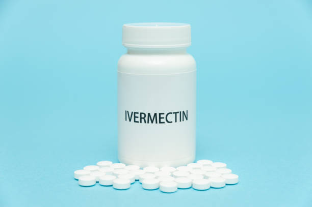 istock Treatments for Coronavirus (COVID-19): IVERMECTIN in white bottle packaging with scattered pills. Isolated on blue background. Horizontal shot 1255914034