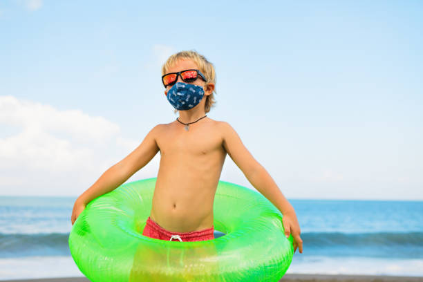 istock Funny child in sunglasses, protective face mask on beach 1255919902
