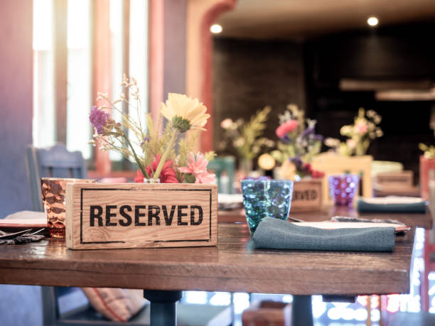 Wooden reserved sign standing with glass and flower pot on dining table in retro style restaurant.