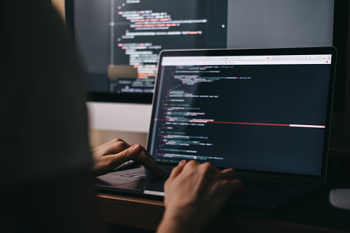 Young caucasian female programmer in glasses writes program code on a laptop computer. home office. High quality photo