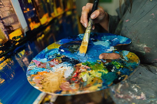 Young Caucasian woman mixes paints on a palette at home art studio