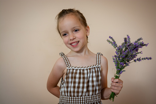Smiling little girl holding lavender flowers indoors