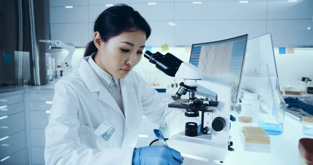 istock Genetic research laboratory interior. Asian female doctor using microscope 1255930565