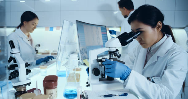 istock Genetic research laboratorr. Asian female doctor using microscope, research partner in background 1255930573