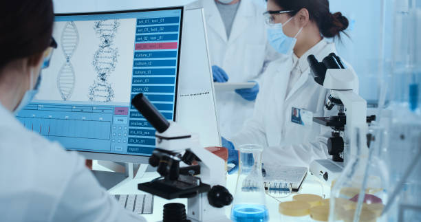 istock Genetic research laboratorr. Asian female doctor using microscope, research partner in background 1255930749