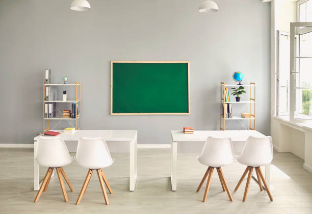 istock Empty school classroom interior with desks and chairs, space for text on chalkboard. Modern schoolroom with furniture 1255931659
