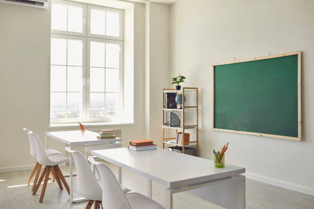 istock White school classroom interior. Bright lassroom with windows tables chair green board 1255931732