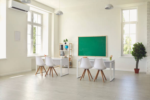 istock Modern empty classroom interior with desks, chairs and chalkboard. Light schoolroom with comfy furniture and big windows 1255931734