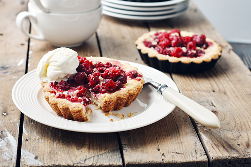 Baked mini pies with raspberries on a rustic wooden table.