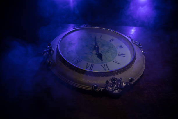 istock Time concept. Big vintage round clock on wooden table with abstract light. 1255934091