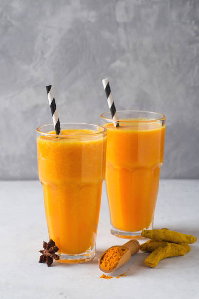 turmeric smoothie in glass with ingredients, turmeric powder, ginger and spice on grey - orange smoothie imagens e fotografias de stock