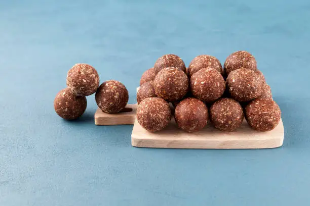 Healthy homemade sweets on a wooden cutting board. Energy balls are a healthy snack. Smooth balls on a blue background, place for text.