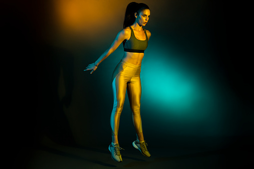 Studio shot of a young sportswoman doing squat jumps.