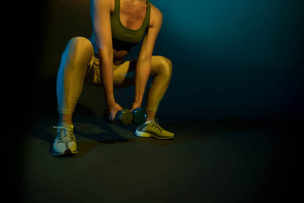 An unrecognizable sportswoman doing squats with dumbbells