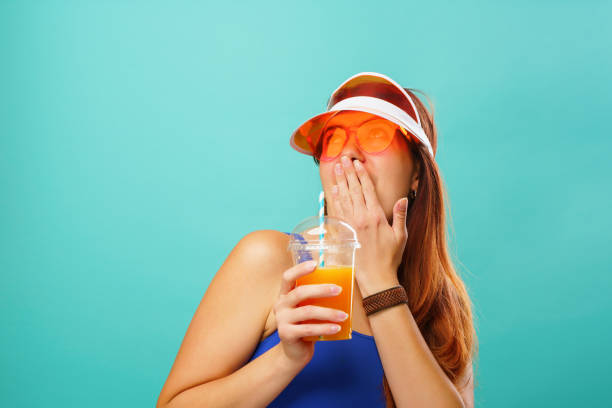 istock Woman wearing a blue swimsuit and hat drinks fruit juice from a cup 1255943149