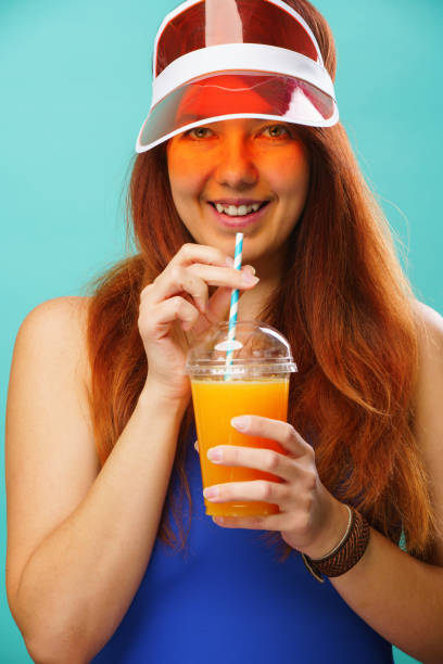 istock Woman wearing a blue swimsuit and hat drinks fruit juice from a cup 1255943310