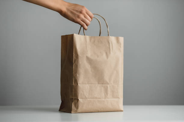istock Hand holds craft eco pack on gray background, mock up. Delivery concept 1255944970