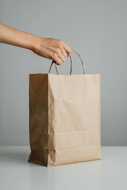 istock Hand holds craft eco pack on gray background, mock up. Delivery concept 1255945080