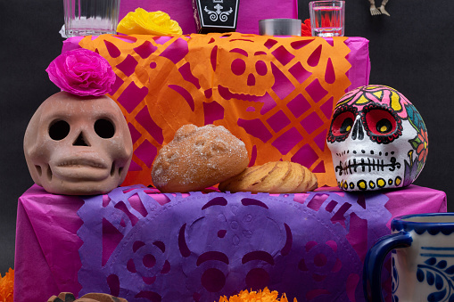 Part of a Mexican Day of the Dead offering altar with skulls, flowers, bread and cut paper on black background