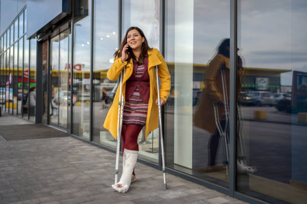 mujer con pie de yeso hablando por teléfono - crutch fotografías e imágenes de stock