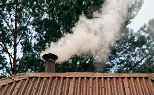 Thick smoke comes out of the chimney into the sky on a background of foliage