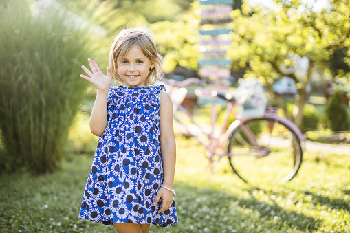Portrait of a happy little girl wearing dress, waving and looking at camera outdoors