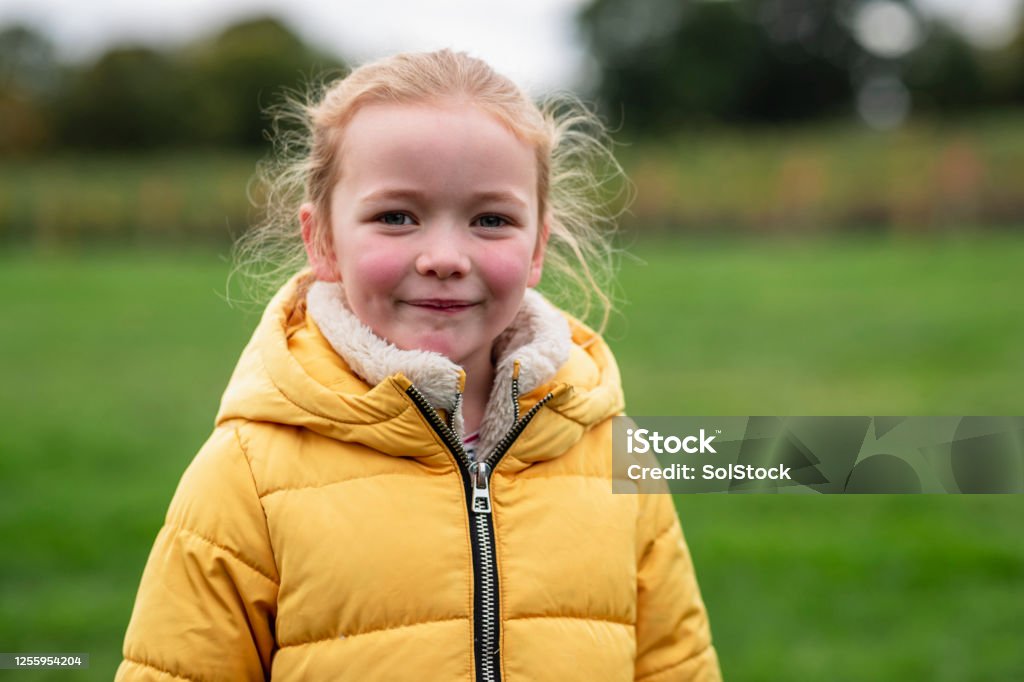 Autumn Portrait Portait of a young girl standing in a field while at a farm in Autumn, smiling while looking at the camera. She is wearing a yellow puffer jacket. Child Stock Photo