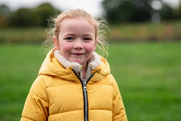 Portait of a young girl standing in a field while at a farm in Autumn, smiling while looking at the camera. She is wearing a yellow puffer jacket.