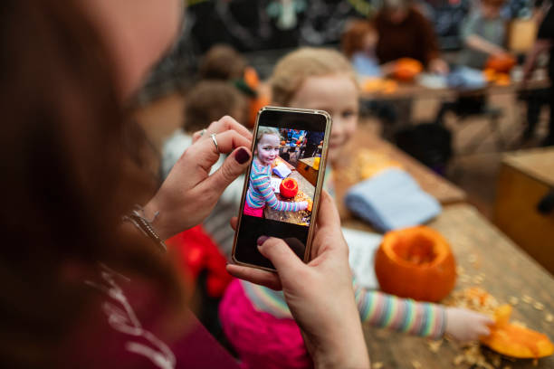 Family Carving Pumpkins Family with children carving pumpkins at a farm after picking them at a farm in preparation for Halloween. A mother is taking a picture of her daughter while she creates her pumpkin. over the shoulder view photos stock pictures, royalty-free photos & images