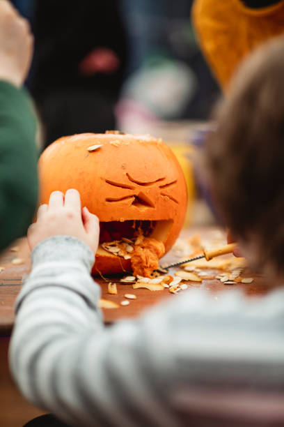 Best Pumpkin Design! Unrecognisable children carving pumpkins at a farm after picking them at a farm in preparation for Halloween. Focus is on a pumpkin that is being carved to look like it is vomiting pumpkin seeds. pumpkin throwing up stock pictures, royalty-free photos & images