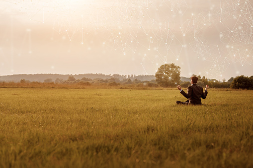 Young businessman meditates in a field on the Internet.