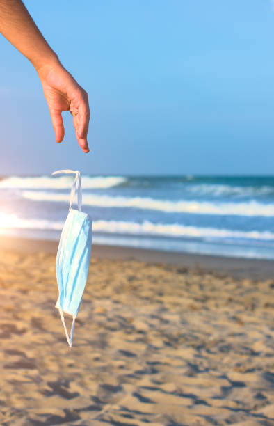 istock Woman's hand dropping coronavirus protective face mask on the beach. 1255962493