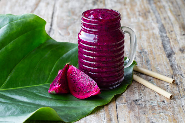 Fresh smoothie juice from a Dragon fruit (pitahaya) in a glass jar, fruit slices, tropical green leaf on old rustic table.