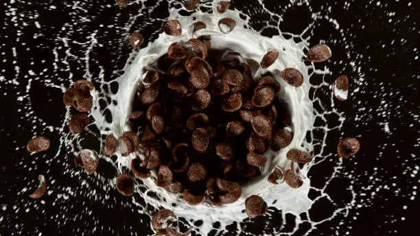 Freeze motion of rotating cereal pieces with milk splash, isolated on black background. Flying food concept, healthy eating.