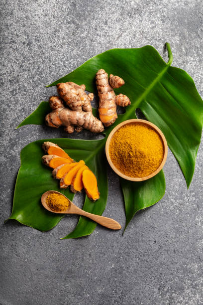 Turmeric powder and fresh turmeric root on grey concrete background. Turmeric powder and fresh turmeric root on grey concrete background with copyspace. Spice, natural coloring, alternative medicine. flora family stock pictures, royalty-free photos & images