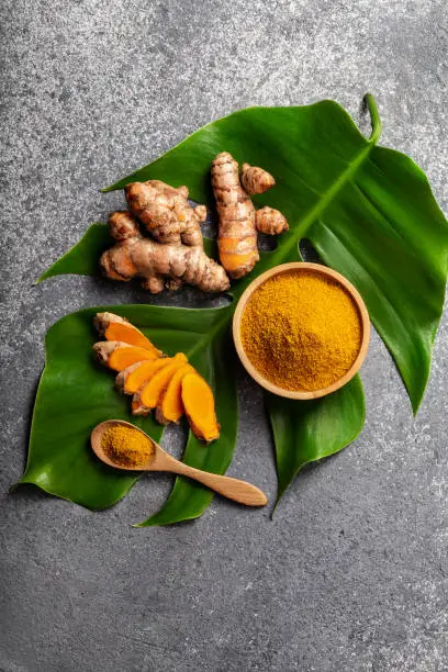 Turmeric powder and fresh turmeric root on grey concrete background with copyspace. Spice, natural coloring, alternative medicine.