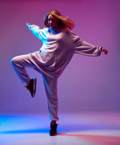 chica joven elegante, baile fresco en una sudadera con capucha con el pelo en desarrollo, sobre un fondo de neón. cartel de la escuela de danza - dancing dancer hip hop jumping fotografías e imágenes de stock