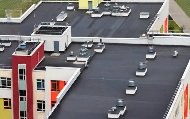 Photo of Top view dark flat roof with air conditioners and hydro insulation membranes on top of a modern apartment building residential area.