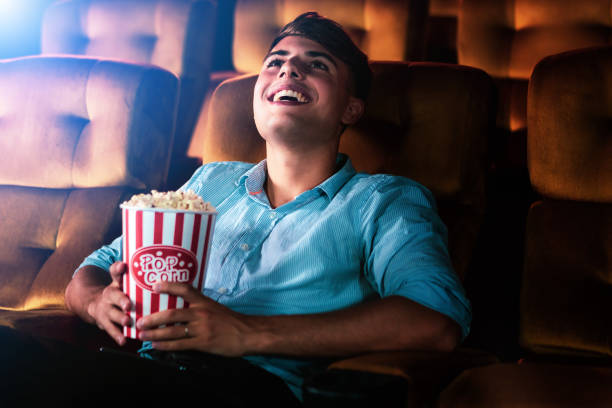 A young man smiling enjoying with his popcorn while watching a movie in theater cinema